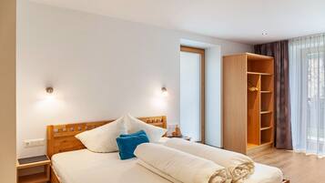Una cama bien hecha con almohadas, una mesita de noche de madera, un armario y una ventana con cortinas.