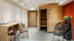 Une salle de spa moderne avec un comptoir d’accueil en bois, deux chaises noires en fil de métal, une cloison en verre et un mur en bois orné d’une petite plante verte.