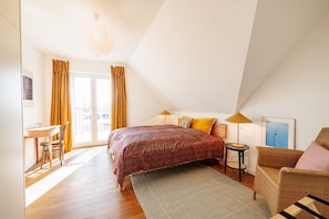 A bedroom with a bed, a desk, a chair, a lamp, and a view of the city.