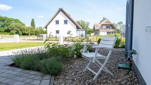 A white building with a sloped roof, a garden with gravel and plants, and a white folding chair. - Ferienhaus Amrai auf der Insel Rügen - Familienurlaub auf der Insel Rügen (Poseritz)