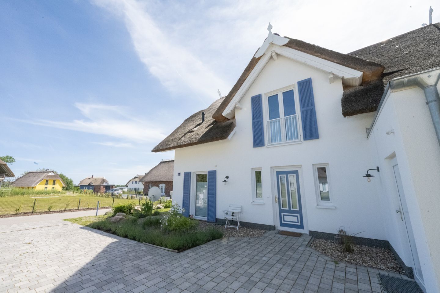 A two-story house with a white facade and blue shutters, a paved driveway, and a small garden area.