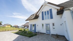 A two-story house with a white facade and blue shutters, a paved driveway, and a small garden area. - Ferienhaus Amrai auf der Insel Rügen - Familienurlaub auf der Insel Rügen (Poseritz)