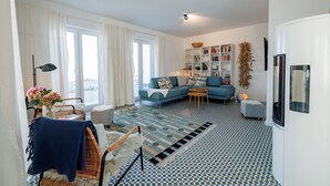 A modern living room with a blue sofa, a bookshelf, and a patterned rug. - Ferienhaus Amrai auf der Insel Rügen - Familienurlaub auf der Insel Rügen (Poseritz)