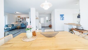 A modern living room with a blue sofa, a wooden dining table, and a kitchen area with a toaster. - Ferienhaus Amrai auf der Insel Rügen - Familienurlaub auf der Insel Rügen (Poseritz)