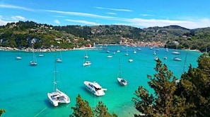 A coastal marina with numerous sailboats docked, surrounded by hills and a small town.