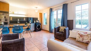 A modern kitchen with a built-in oven, a washing machine, and a dining area with blue chairs. - House with View, Shared Pool and Garden (Lacanau-Ocean)
