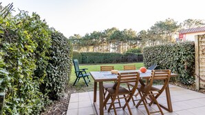 A patio with a table and chairs, surrounded by hedges and a view of a garden. - House with View, Shared Pool and Garden (Lacanau-Ocean)
