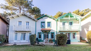 A two-story house with a balcony, a patio with a table and chairs, and a well-maintained lawn. - House with View, Shared Pool and Garden (Lacanau-Ocean)