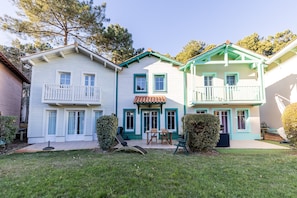 A two-story house with a balcony, a patio with a table and chairs, and a well-maintained lawn. - House with View, Shared Pool and Garden (Lacanau-Ocean)