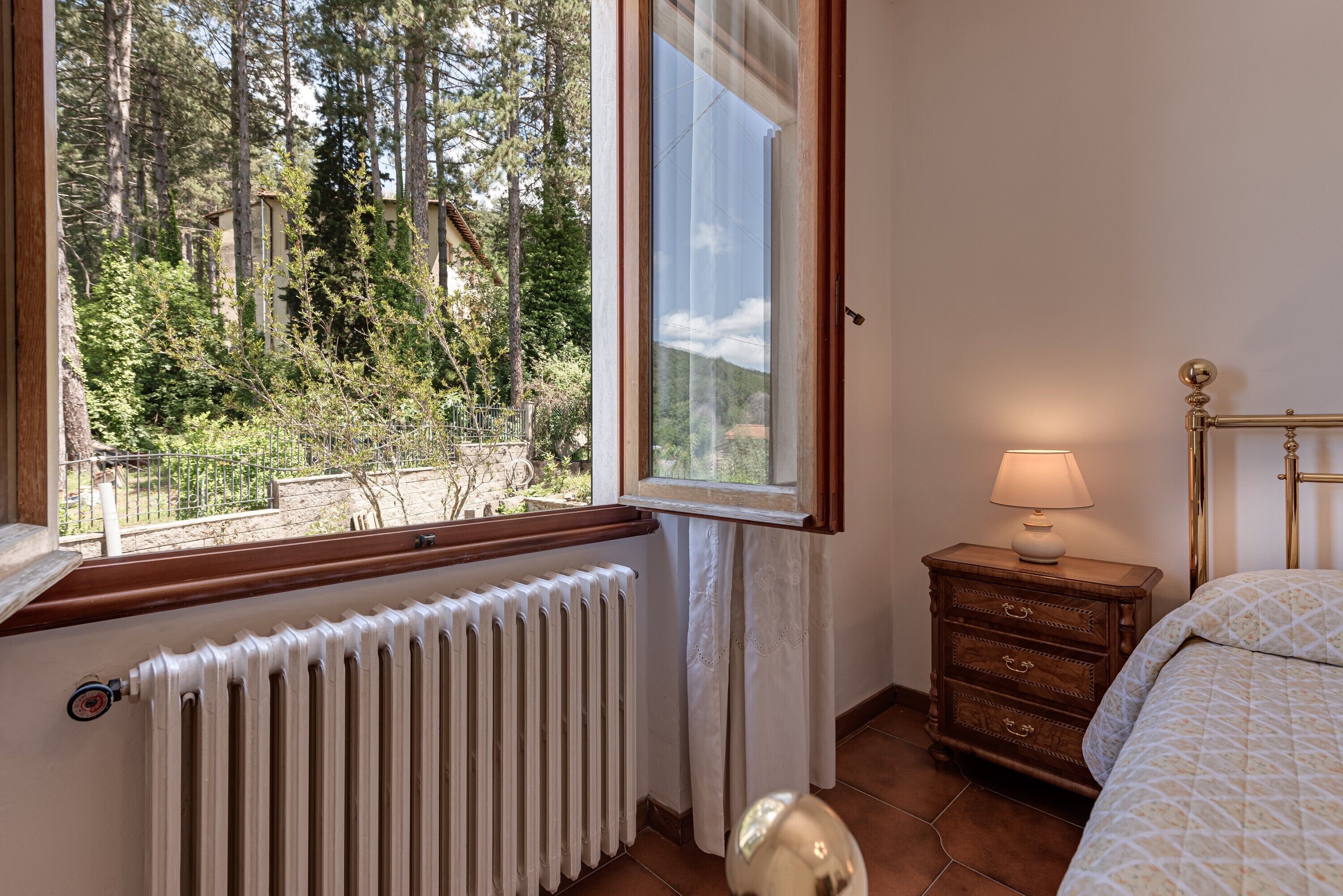 A bedroom with a window, radiator, wooden dresser, and a lamp.