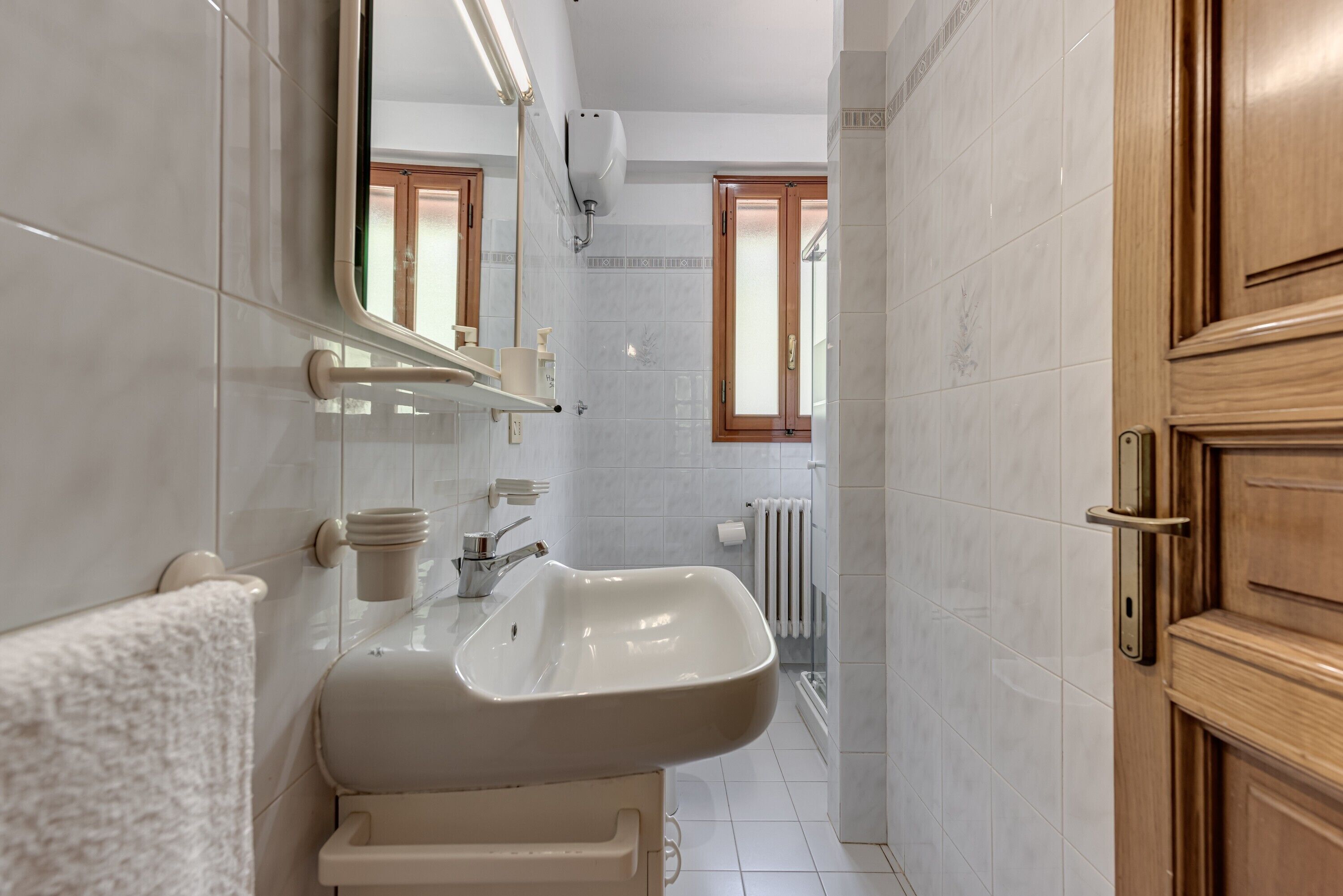 A bathroom with a sink, mirror, towel rack, and a wooden door.