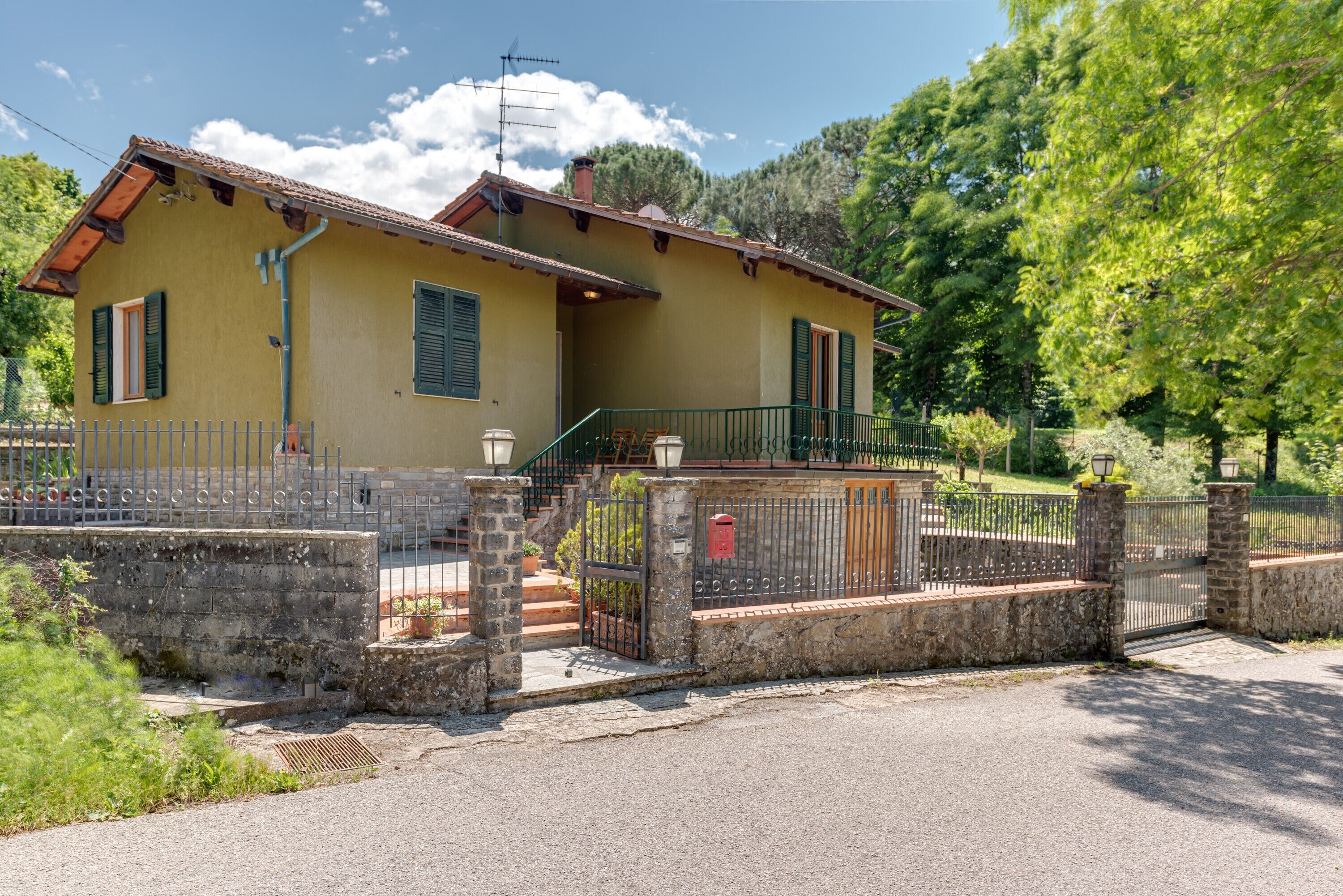 A yellow house with a balcony, a stone wall, and a metal gate.