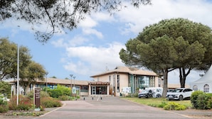 A building with a tiled roof, a large tree, and parked cars. - Holiday Apartment "Résidence moderne avec piscine" with Shared Pool, Terrace & Wi-Fi (Moliets-et-Maa)