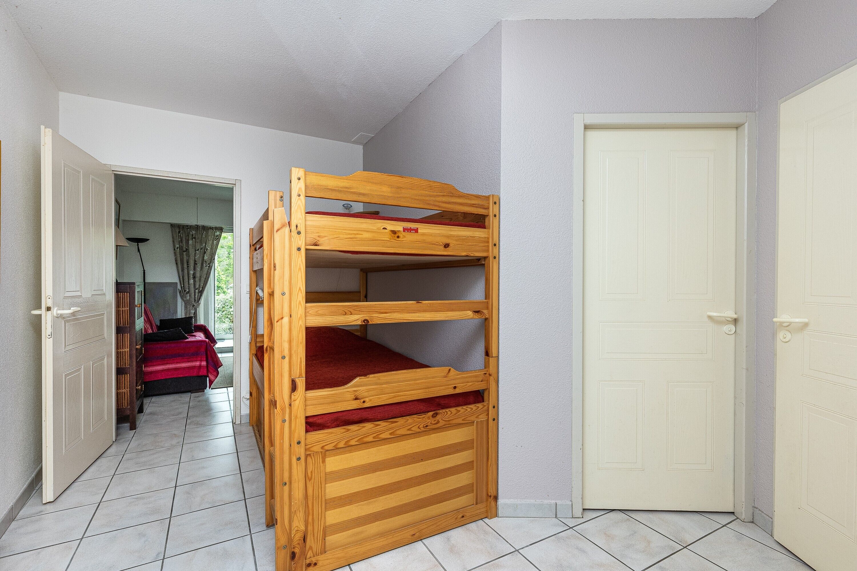 A bunk bed in a room with a door, a window, and a hallway leading to another room.