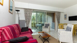 A living room with a red sofa, a wicker chair, a wooden coffee table, and a television on the wall. - Holiday Apartment "Résidence moderne avec piscine" with Shared Pool, Terrace & Wi-Fi (Moliets-et-Maa)