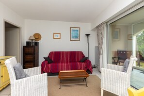 En stue med en rød-stribet sofa, to hvide fletstole, et træsofabord, et gult skab og en gulvlampe.