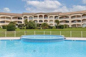 Et hotel med swimmingpool, flere balkoner og en velholdt græsplæne.