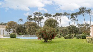 A well-maintained lawn with a small tree, a swimming pool, and tall trees in the background. - Holiday Apartment "Résidence moderne avec piscine" with Shared Pool, Terrace & Wi-Fi (Moliets-et-Maa)