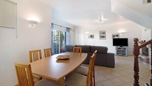 A dining area with a wooden table and chairs, a grey sofa, a flat-screen TV, and a staircase. - "Villa Catarina" Vacation Home with Pool & Wi-Fi (Albufeira)
