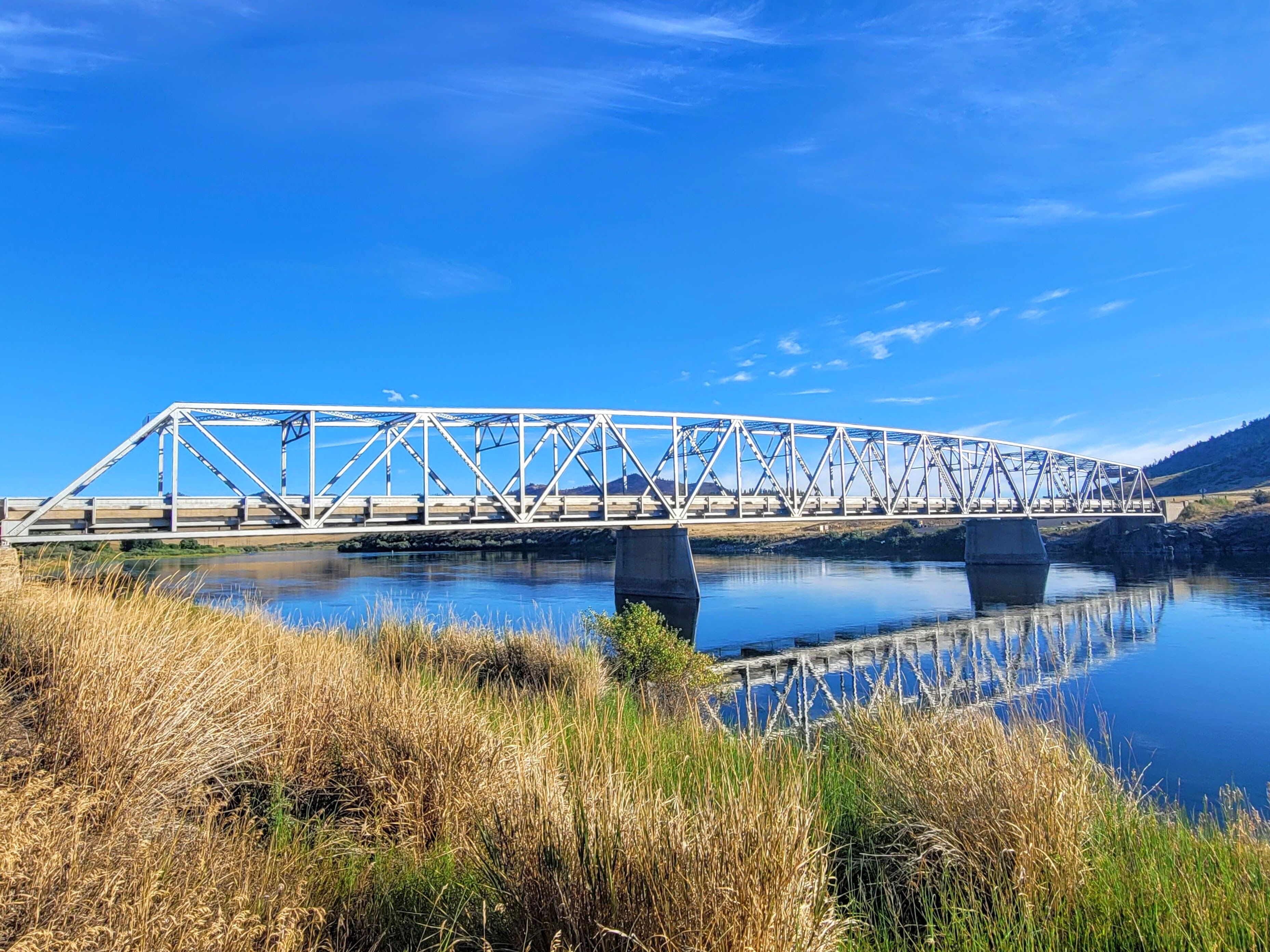 Eine Stahlbrücke über einem ruhigen Fluss mit grünen Ufern.