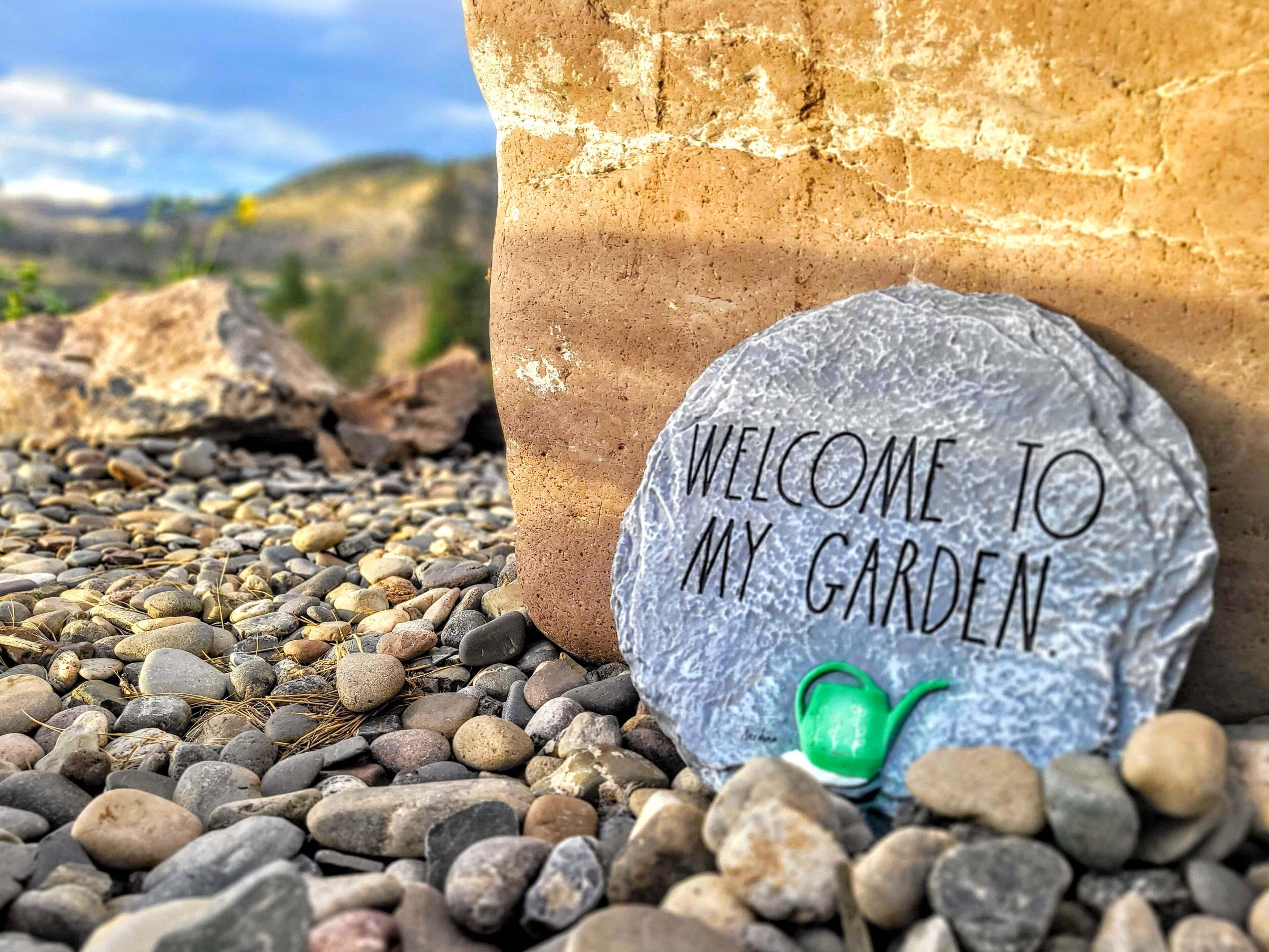 Un letrero de bienvenida en un jardín con muro de piedra y guijarros.