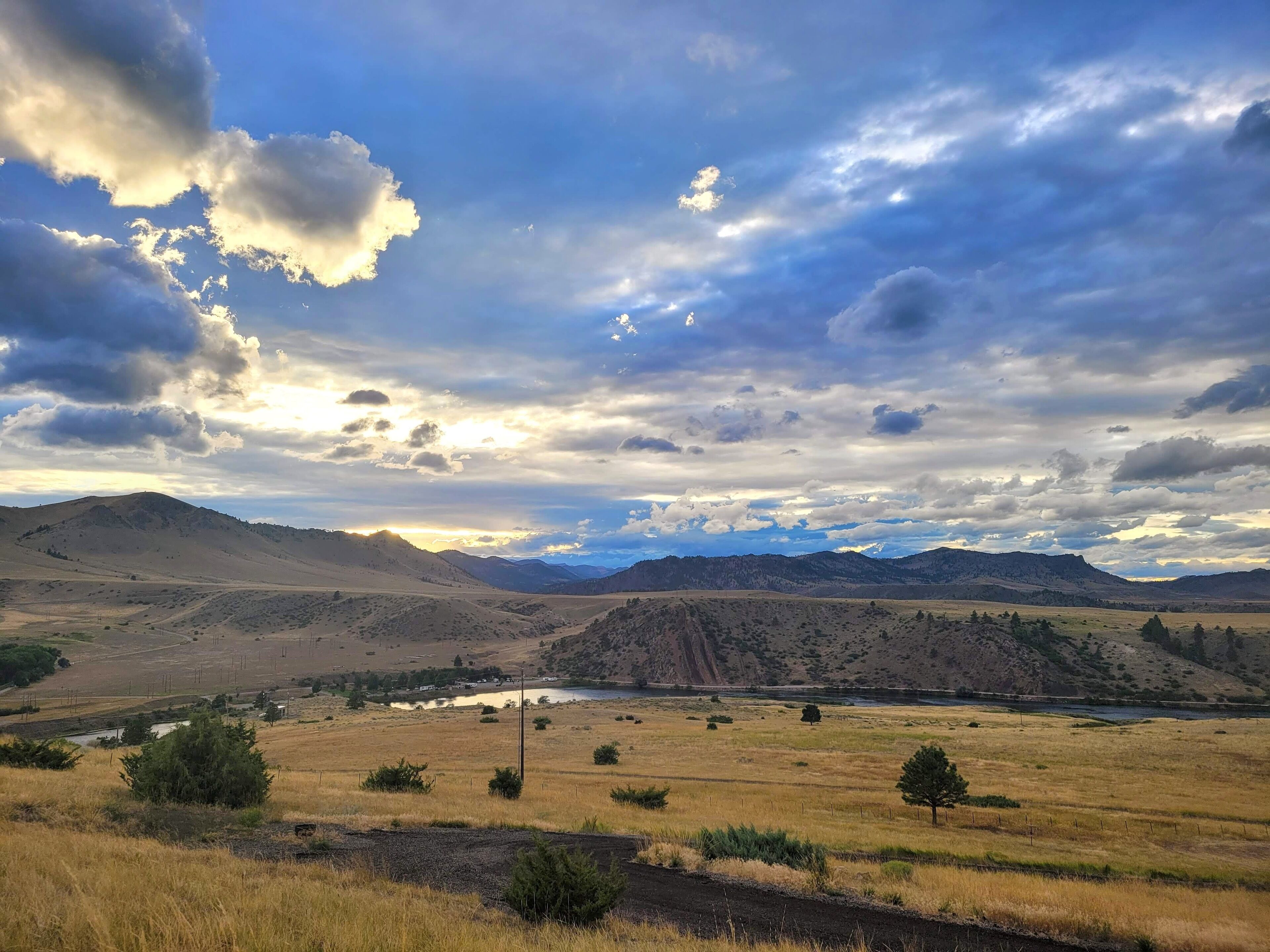 A wide-open landscape with a river, distant mountains, and a cloudy sky.