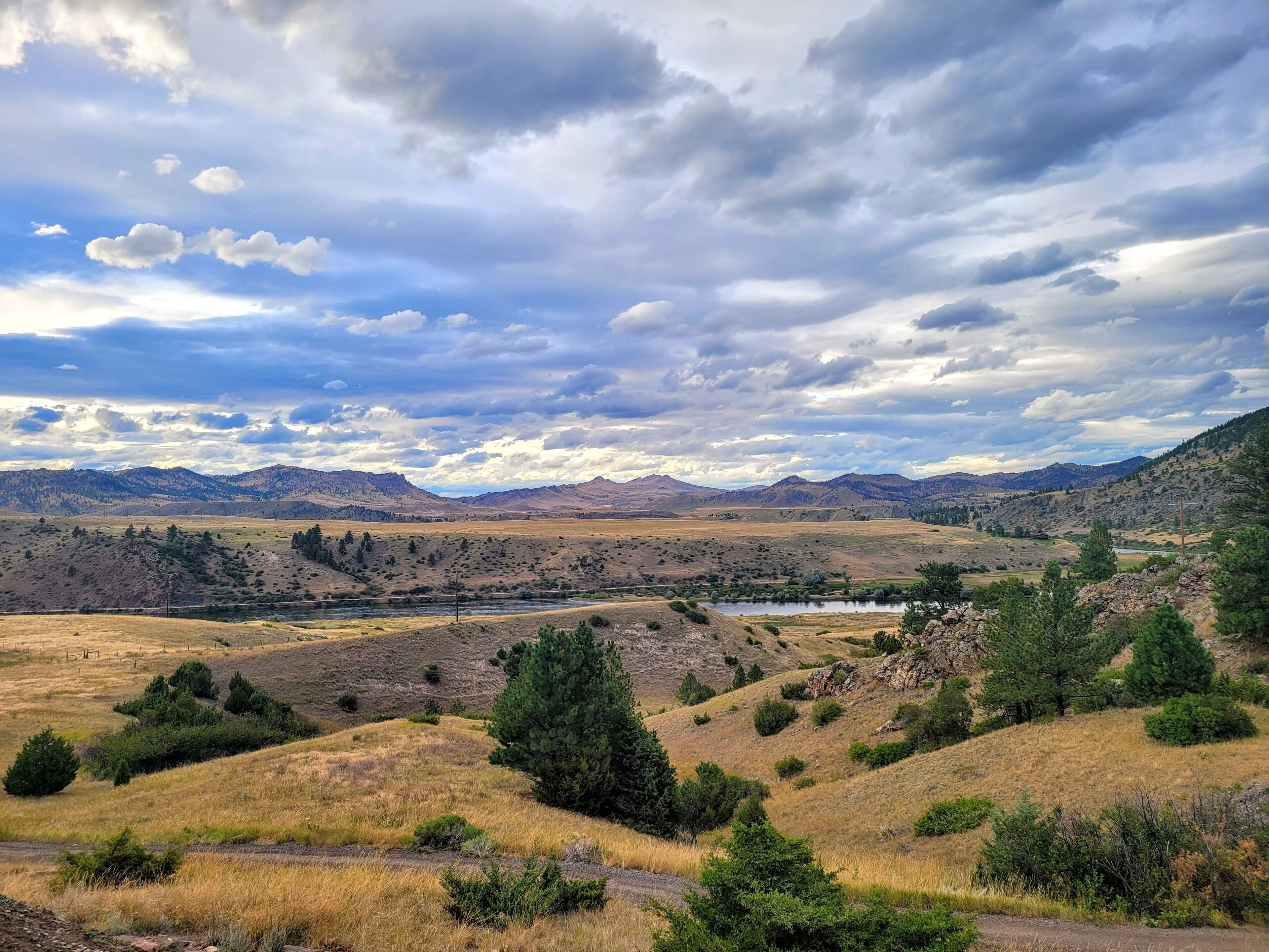 A landscape with rolling hills, a river, and a cloudy sky.