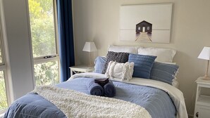 Une chambre à coucher avec un grand lit, deux tables de chevet, une fenêtre avec des rideaux et un tableau accroché au mur.