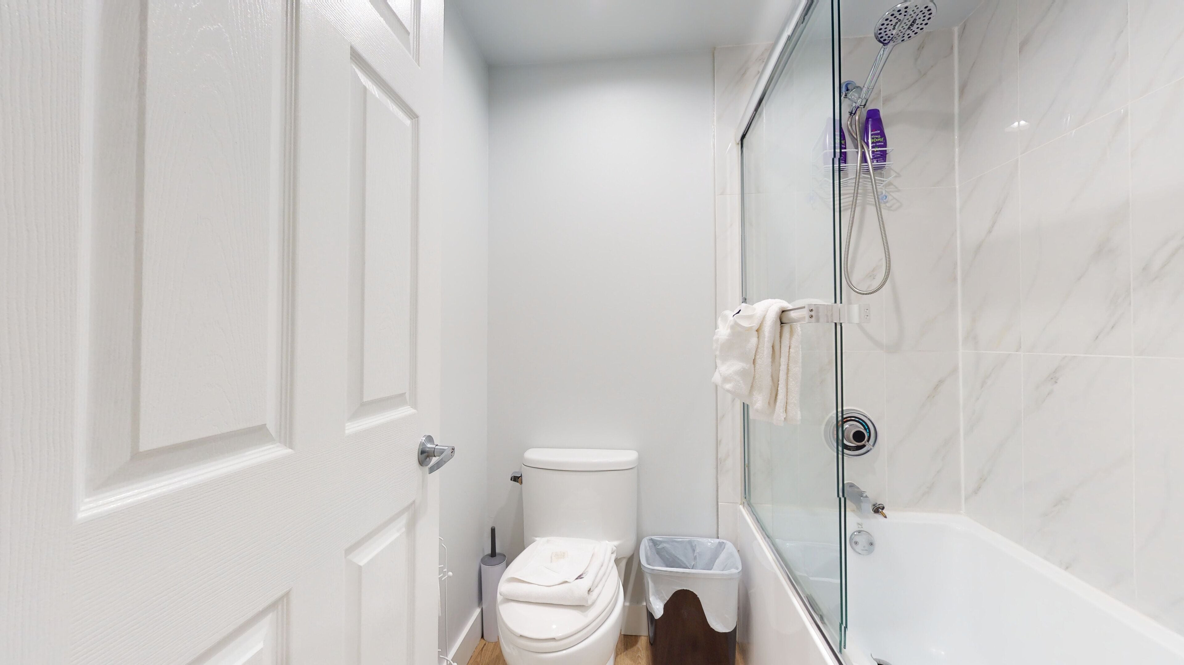 Un bagno con un water, cabina doccia in vetro e un cestino.