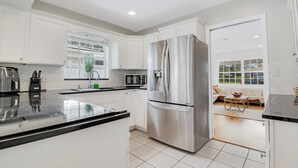 Una cocina moderna con armarios blancos, electrodomésticos de acero inoxidable y vistas a una sala de estar.