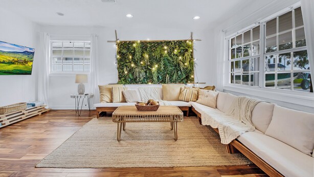 Una sala de estar moderna con un sofá seccional grande, una mesa de centro de ratán y un jarrón de plantas montado en la pared.