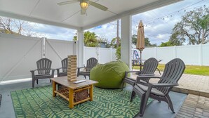 Un patio techado con ventilador de techo, asientos exteriores y un tapete verde estampado.