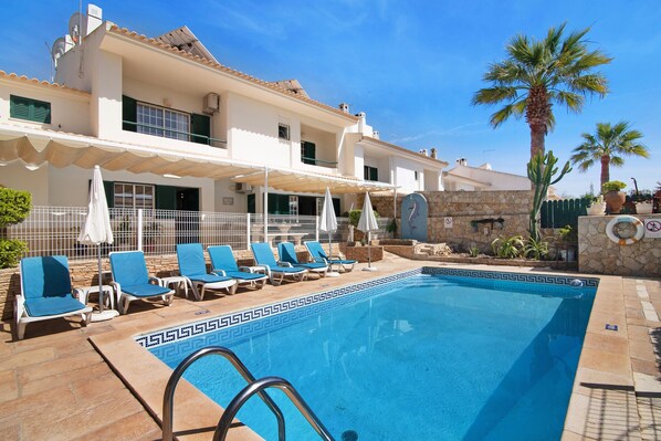A swimming pool with lounge chairs, a stone wall, and a palm tree. - Holiday Home "Villa Guisado" with Pool, Terraces & Wi-Fi (Albufeira)