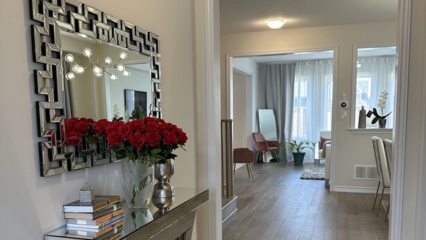 Un soggiorno moderno con un grande specchio, un tavolo consolle con libri e un vaso di rose rosse, e un pavimento in legno.