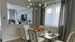 Zona pranzo con tavolo in vetro, sedie bianche e un lampadario.