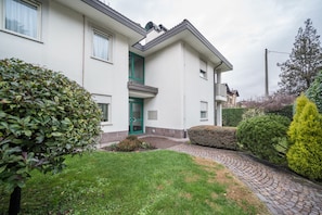 Un immeuble résidentiel à deux étages, avec une porte verte, une allée pavée et des jardins bien entretenus.