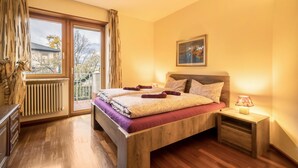 A bedroom with a wooden bed, a nightstand with a lamp, a window with curtains, and a radiator. - Holiday Apartment "Sweet Dreams" with Mountain View, Balcony and Wi-Fi (Merano)