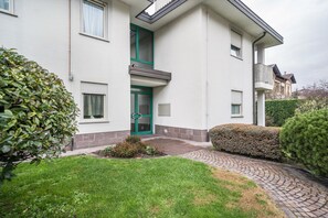 Un bâtiment à deux étages avec une porte verte, un petit jardin et un chemin pavé menant à l’entrée.