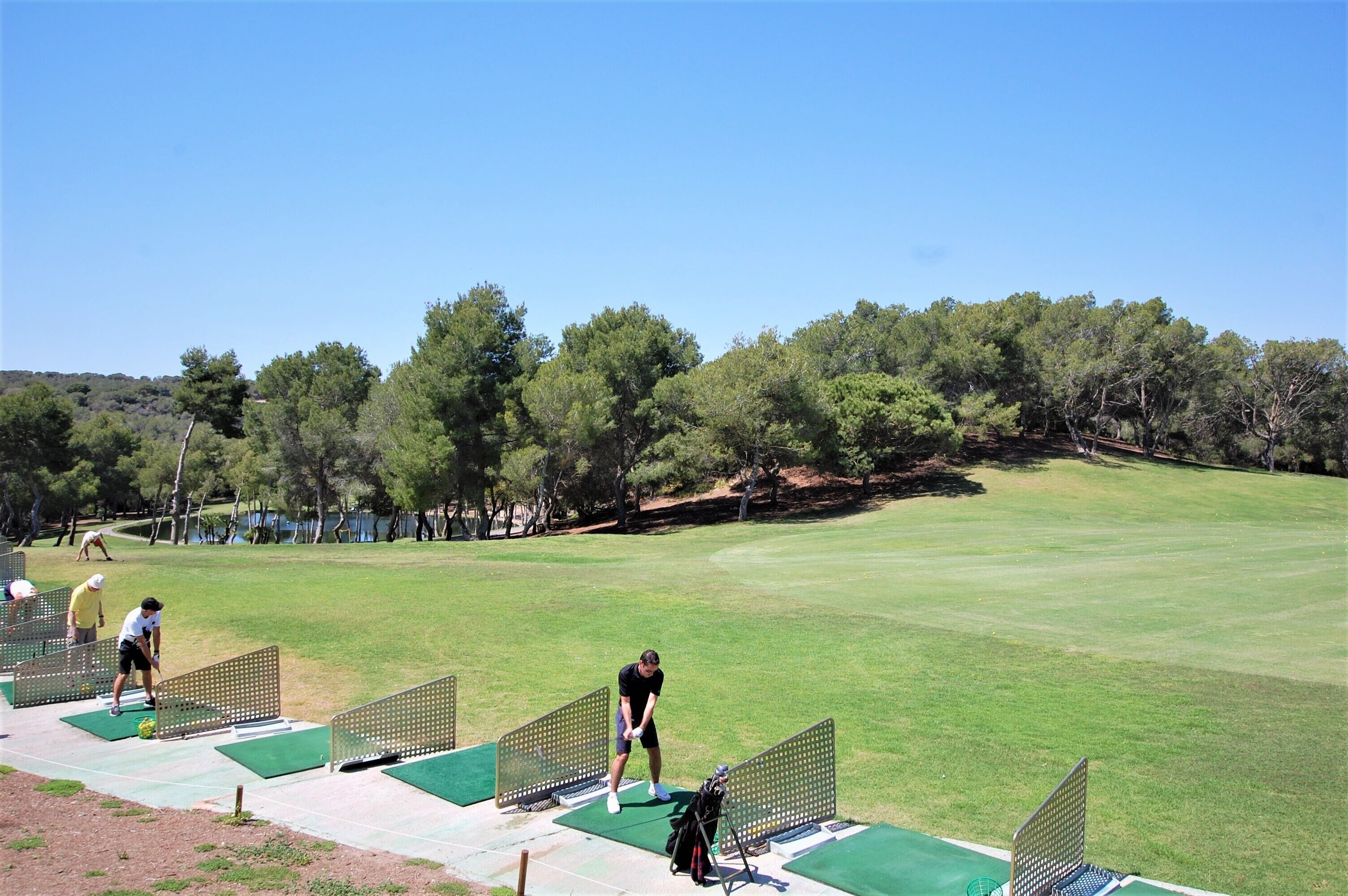 Un campo de golf con cielo despejado, árboles y un césped bien cuidado.