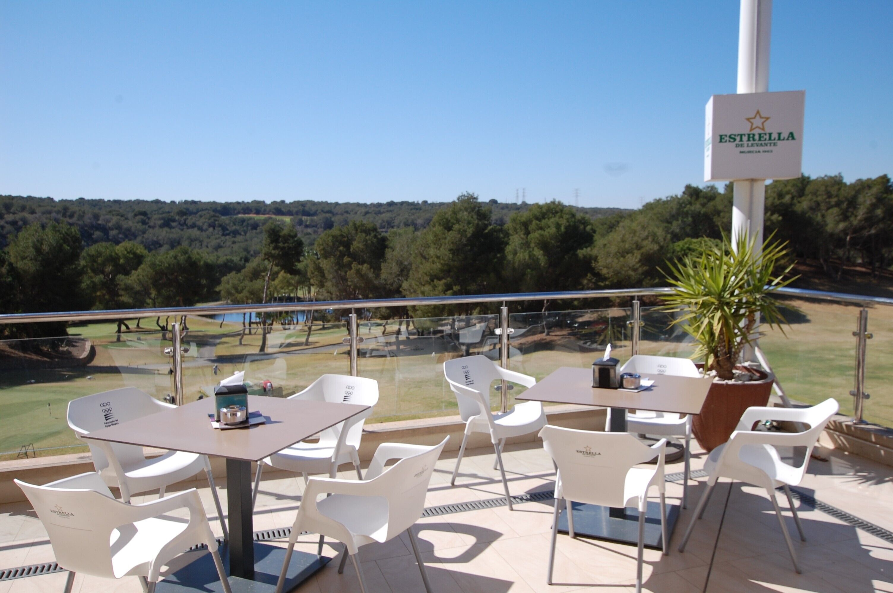 A terrace with outdoor seating, a view of a golf course, and a sign for 'Estrella de Levante'.