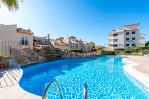 Une piscine à l’eau d’un bleu cristallin, entourée de murs en pierre et d’une clôture en métal.