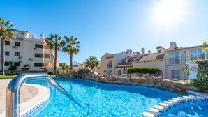 A swimming pool with a stone border, palm trees, and buildings in the background. - Holiday Apartment "Sunnygolfbeach" with Shared Pool, Terraces & Wi-Fi (Orihuela Costa)