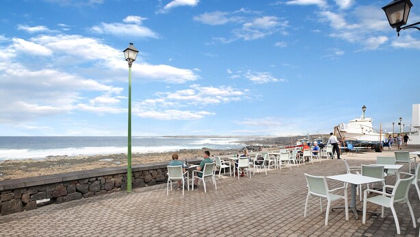 A seaside patio with tables and chairs, a stone wall, and a view of the ocean. - Holiday Home "Casa Lía" with Wi-Fi (La Santa)