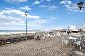 A seaside patio with tables and chairs, a stone wall, and a view of the ocean.