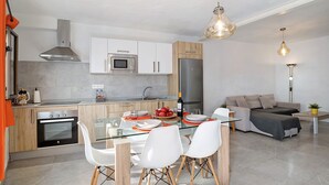 A modern kitchen with a glass dining table, white chairs, a built-in oven, and a stainless steel refrigerator. - Holiday Home "Casa Lía" with Wi-Fi (La Santa)