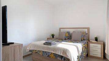 Un dormitorio con cama, mesitas de noche, televisor y una planta pequeña.
