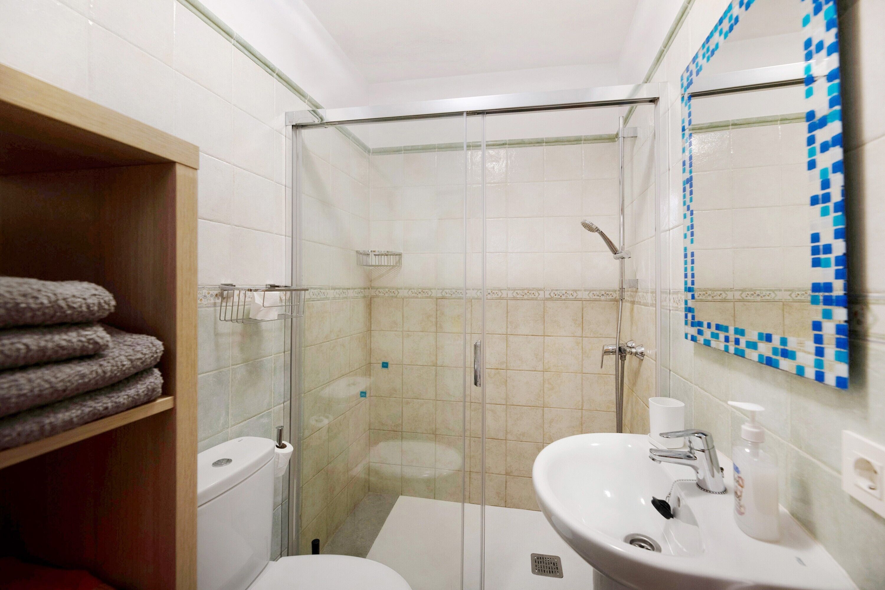 A bathroom with a glass-enclosed shower, a toilet, a sink with a mirror, and a towel rack.