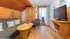 Ein Zimmer mit Holzwänden, ausgestattet mit einer Couch, einem Sessel, einem Couchtisch, einem Fernseher und einer Tür, die nach draußen führt.