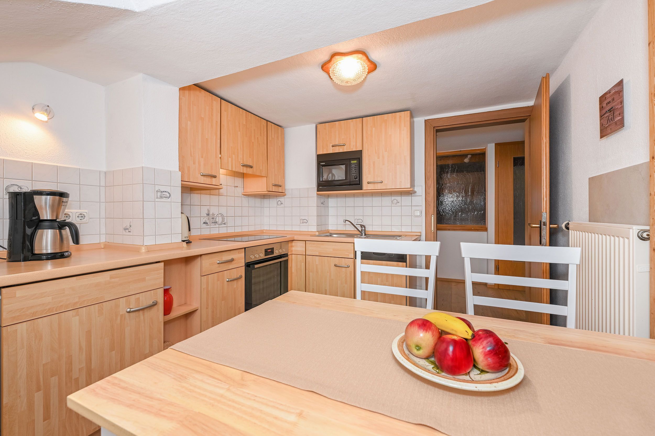 A compact kitchen with wooden cabinets, a microwave, a coffee maker, and a fruit bowl on the counter.