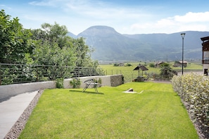 A well-maintained lawn with a swing set, a stone wall, and a view of distant mountains.